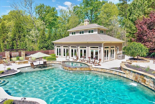 view of pool with french doors, a pool with connected hot tub, fence, a patio, and a fire pit
