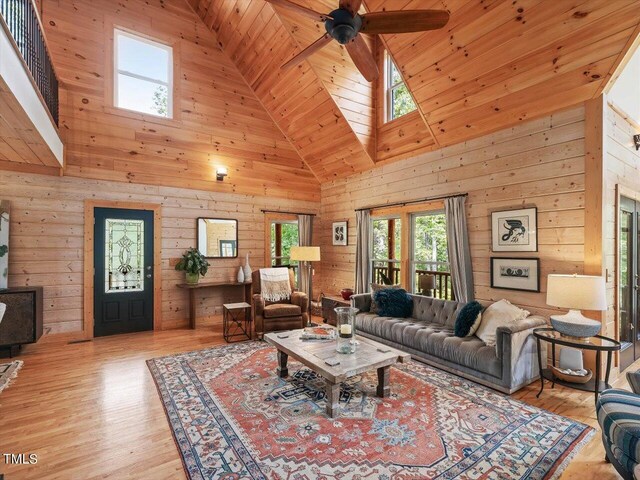 living area with wood finished floors, ceiling fan, wooden walls, high vaulted ceiling, and a skylight