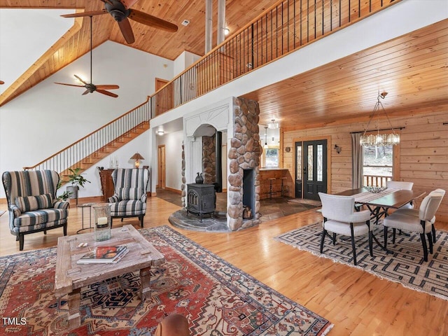 living room with a wood stove, high vaulted ceiling, wood ceiling, and ceiling fan with notable chandelier