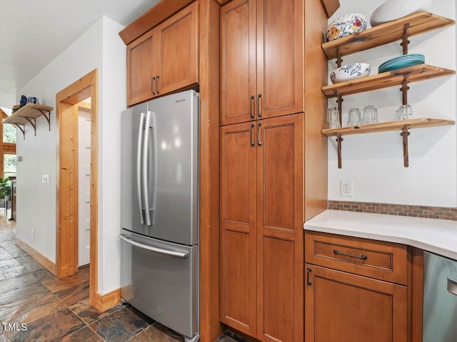 kitchen featuring open shelves, brown cabinets, light countertops, stone tile flooring, and stainless steel fridge