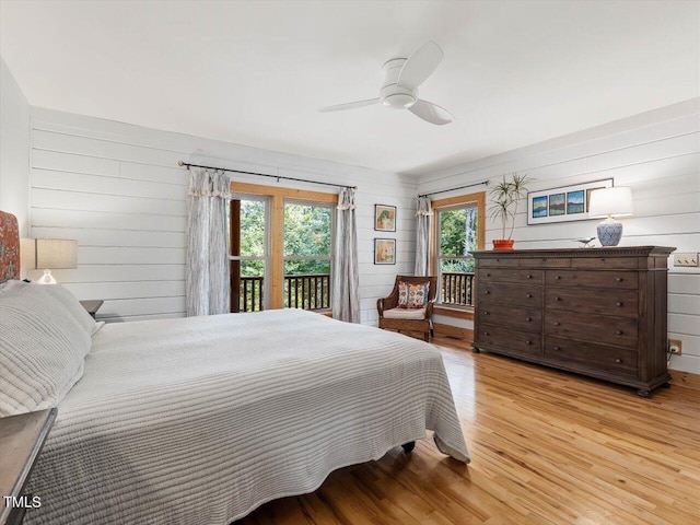 bedroom with a ceiling fan, wood walls, access to exterior, and light wood-style floors