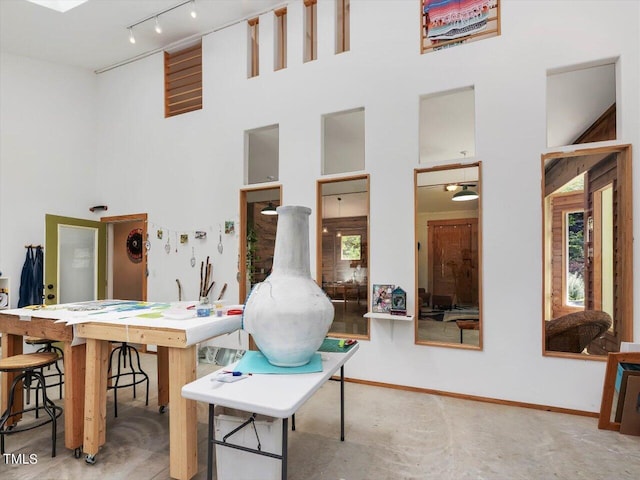 office space featuring track lighting, baseboards, and a towering ceiling