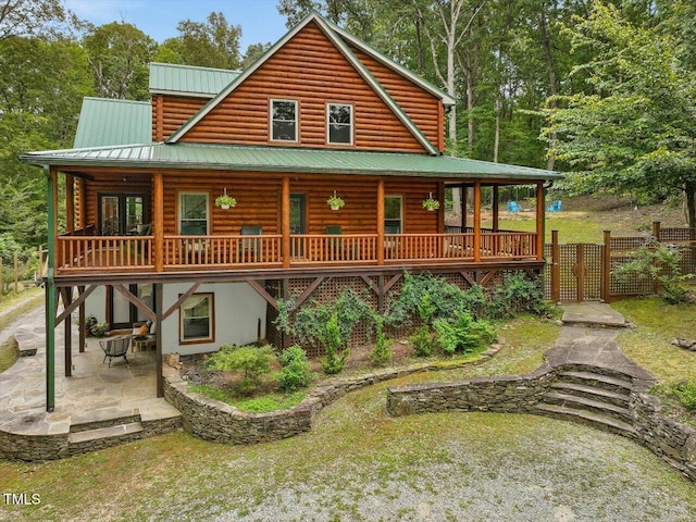 rear view of house with a patio area, fence, log exterior, and metal roof