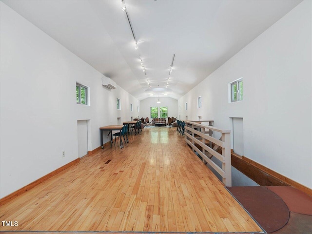 misc room featuring track lighting, lofted ceiling, hardwood / wood-style floors, a wall mounted air conditioner, and an upstairs landing