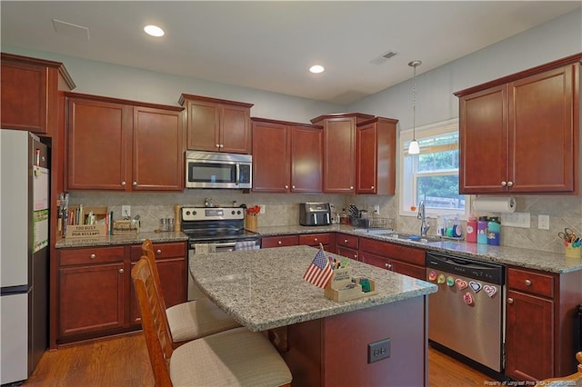 kitchen featuring stainless steel appliances, a sink, wood finished floors, a breakfast bar area, and recessed lighting