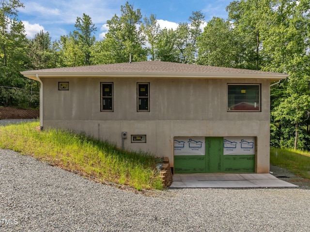 view of home's exterior featuring gravel driveway, an attached garage, view of scattered trees, and roof with shingles