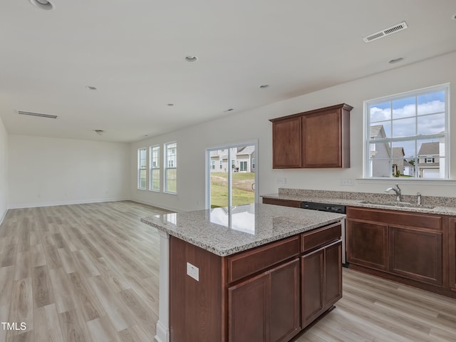 kitchen featuring light wood finished floors, light stone countertops, a sink, visible vents, and a kitchen island