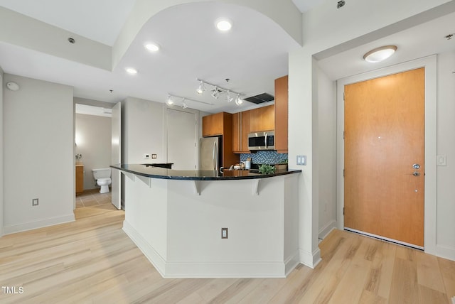 kitchen with light wood finished floors, brown cabinets, a kitchen bar, dark countertops, and appliances with stainless steel finishes