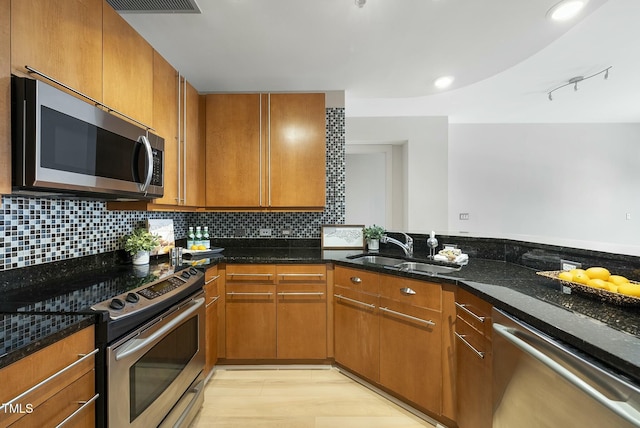 kitchen featuring dark stone countertops, a sink, appliances with stainless steel finishes, and decorative backsplash