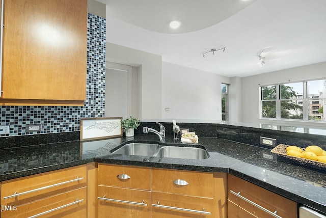 kitchen featuring dark stone counters, brown cabinets, tasteful backsplash, and a sink