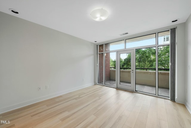 spare room featuring baseboards, visible vents, light wood finished floors, and floor to ceiling windows