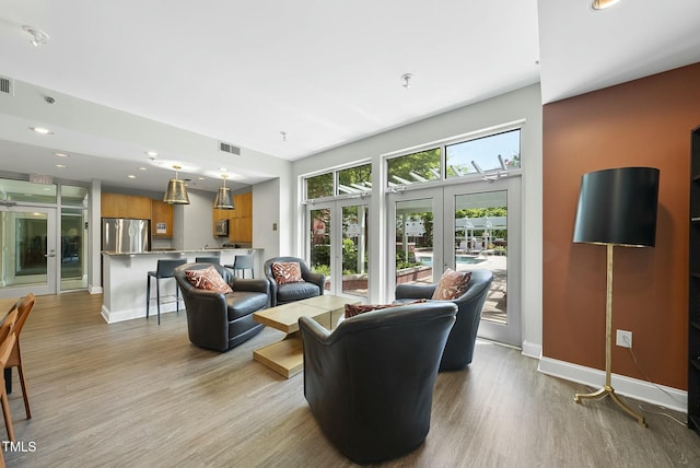 living area with baseboards, visible vents, french doors, and light wood finished floors