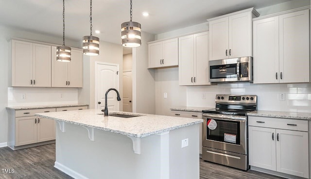 kitchen with a kitchen island with sink, stainless steel appliances, backsplash, a sink, and dark wood-style floors