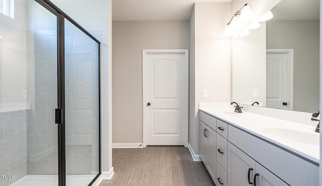 bathroom with baseboards, a stall shower, double vanity, and a sink