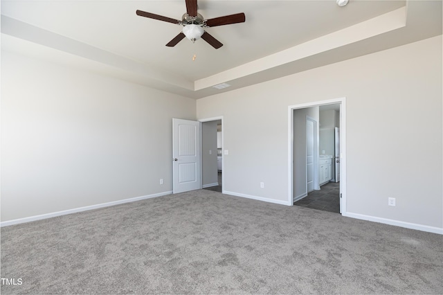 unfurnished bedroom featuring baseboards, a raised ceiling, carpet floors, and ensuite bathroom