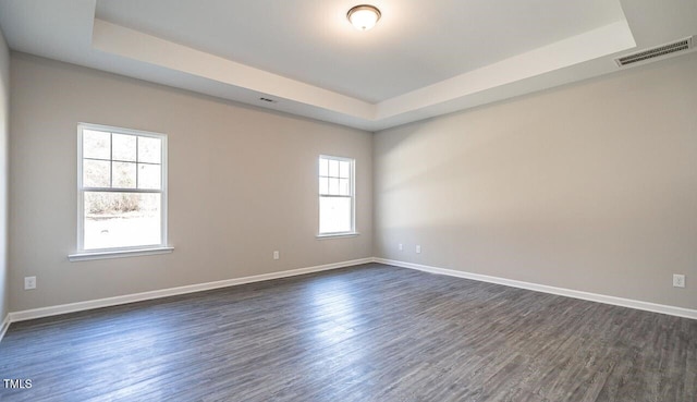 unfurnished room with baseboards, visible vents, dark wood-style flooring, and a tray ceiling