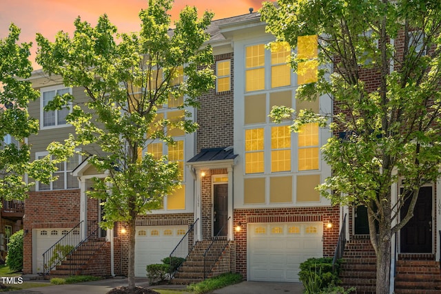 townhome / multi-family property featuring stairway, brick siding, a garage, and a standing seam roof