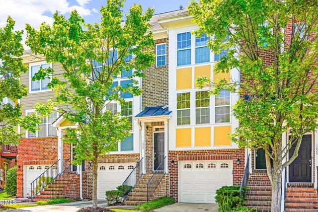 townhome / multi-family property with an attached garage, brick siding, stairway, and driveway
