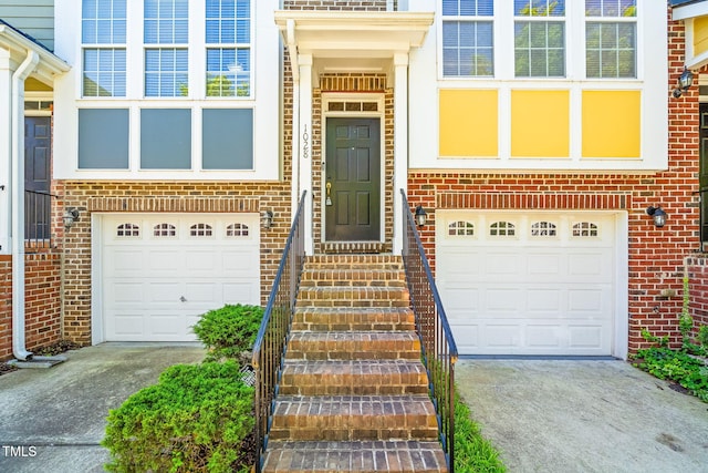 property entrance with a garage, concrete driveway, and brick siding