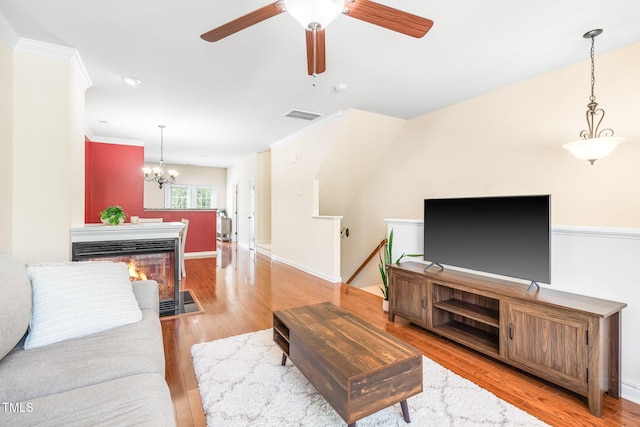 living area with light wood-type flooring, a ceiling fan, a chandelier, ornamental molding, and a multi sided fireplace