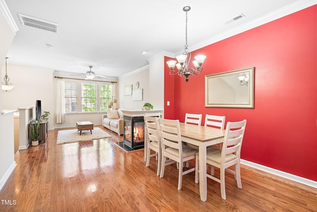 dining room with wood finished floors, ornamental molding, baseboards, a multi sided fireplace, and a ceiling fan