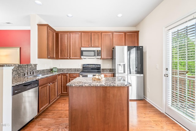 kitchen with stainless steel appliances, a sink, stone countertops, a center island, and light wood-style floors