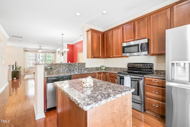 kitchen featuring appliances with stainless steel finishes, crown molding, light wood-style floors, stone countertops, and ceiling fan