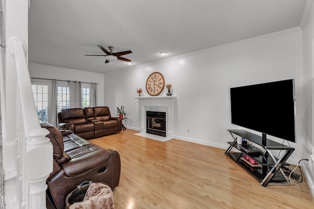 living area with a ceiling fan, wood finished floors, a fireplace with flush hearth, crown molding, and baseboards
