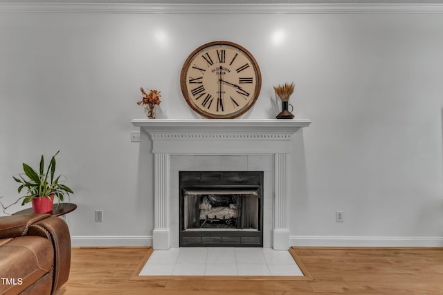 detailed view of wood finished floors, baseboards, a tiled fireplace, and crown molding