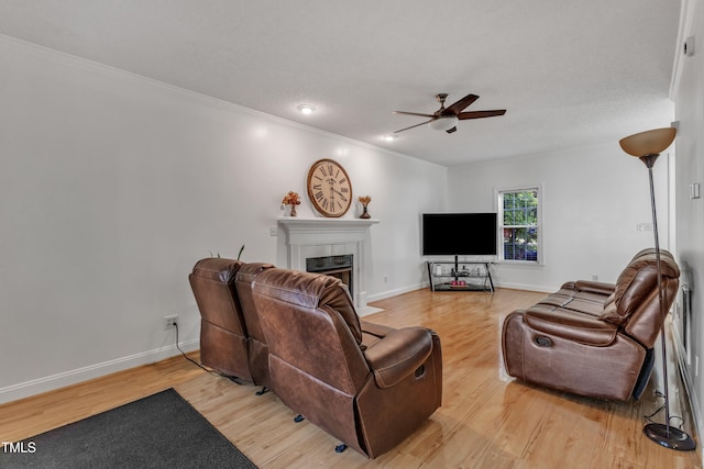 living area featuring ceiling fan, a fireplace, light wood-type flooring, ornamental molding, and baseboards
