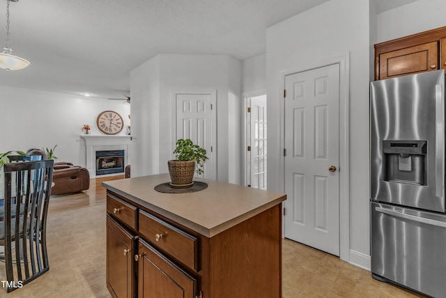 kitchen with stainless steel fridge with ice dispenser, ceiling fan, a center island, a fireplace, and decorative light fixtures