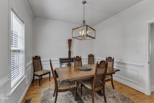 dining room with plenty of natural light, a chandelier, light wood-style floors, wainscoting, and ornamental molding