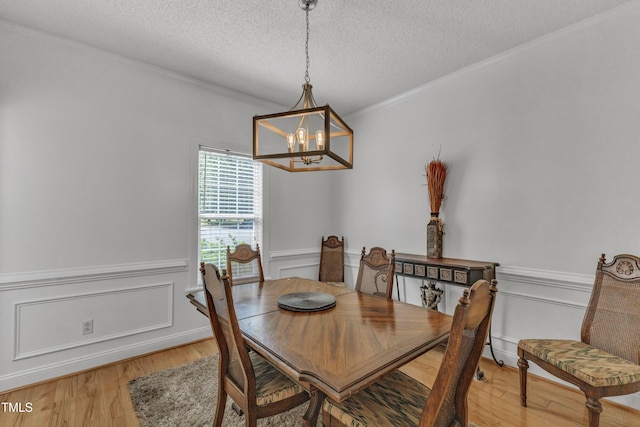 dining room with a chandelier, light wood-type flooring, a textured ceiling, wainscoting, and crown molding