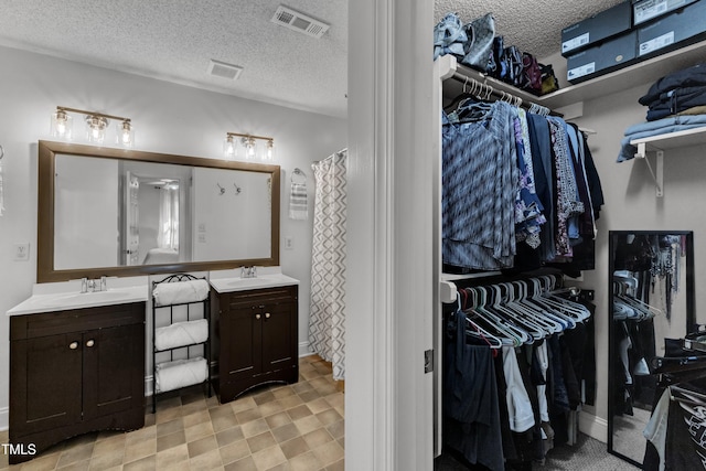 full bath with two vanities, a textured ceiling, and a walk in closet