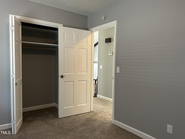 unfurnished bedroom featuring baseboards, a closet, dark colored carpet, and a textured ceiling