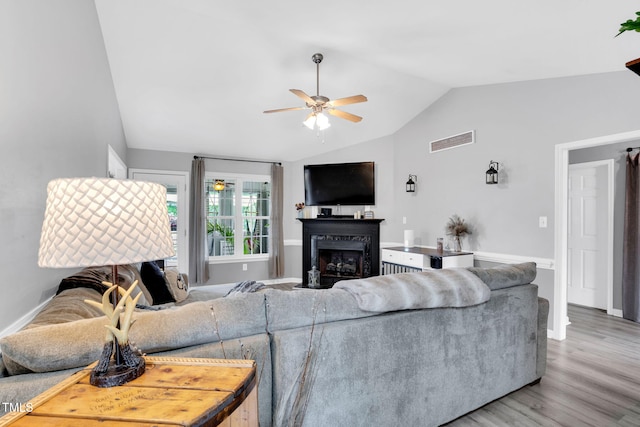 living area featuring a ceiling fan, visible vents, a fireplace, vaulted ceiling, and light wood finished floors