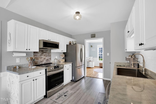 kitchen with appliances with stainless steel finishes, a sink, white cabinetry, decorative backsplash, and light wood-type flooring