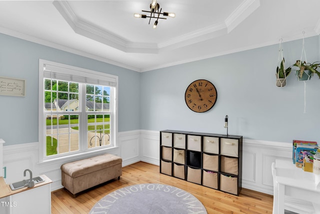 living area featuring an inviting chandelier, ornamental molding, wainscoting, a tray ceiling, and light wood-style flooring