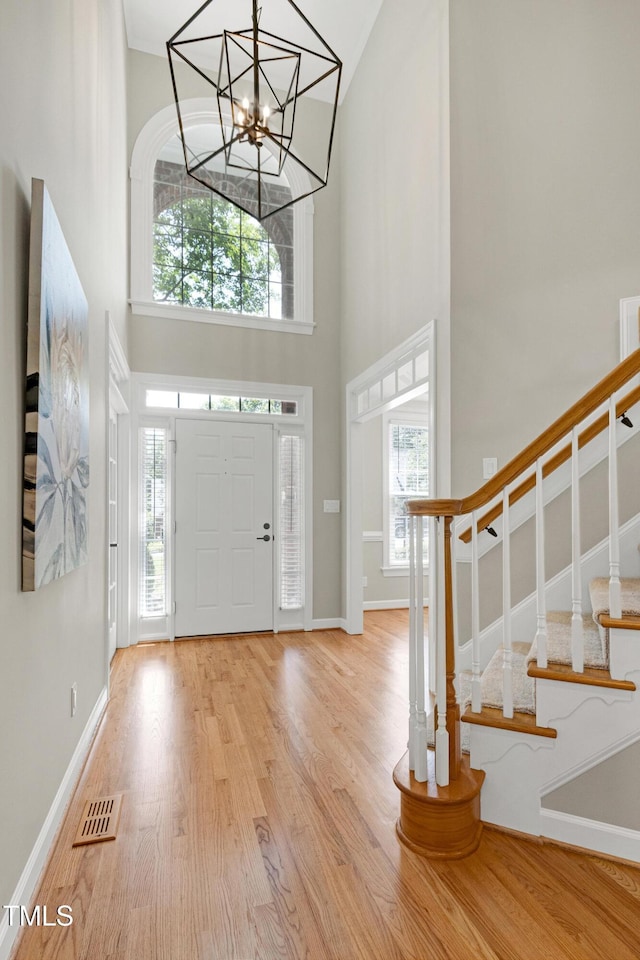 entrance foyer featuring stairs, baseboards, wood finished floors, a towering ceiling, and visible vents