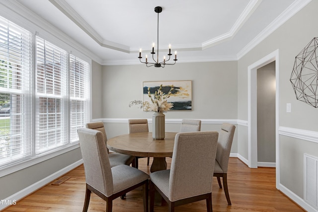 dining space featuring a chandelier, light wood-type flooring, a tray ceiling, visible vents, and ornamental molding