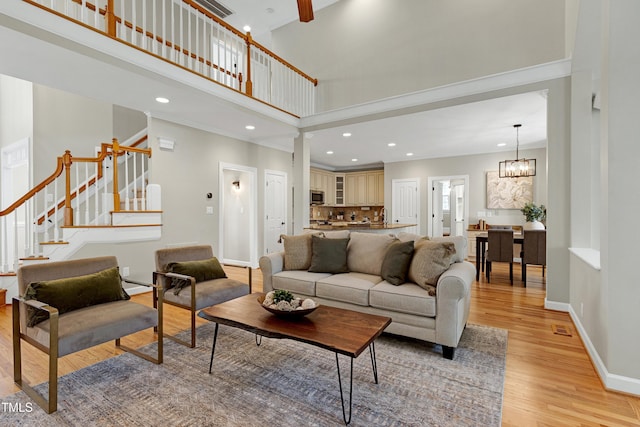 living room featuring a high ceiling, an inviting chandelier, light wood finished floors, baseboards, and stairway