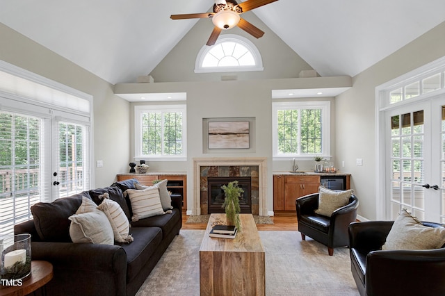 living area with a ceiling fan, french doors, a fireplace, high vaulted ceiling, and light wood finished floors