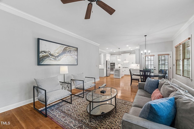 living room with crown molding, baseboards, light wood-type flooring, recessed lighting, and ceiling fan with notable chandelier