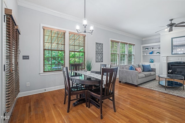 dining room with crown molding, baseboards, a glass covered fireplace, and wood finished floors