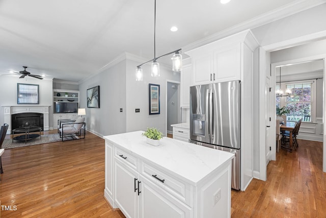 kitchen with crown molding, stainless steel fridge, a fireplace, ceiling fan with notable chandelier, and light wood-type flooring