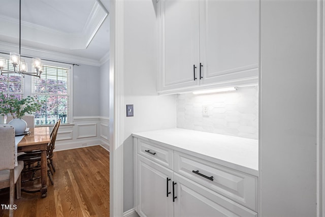 kitchen featuring crown molding, dark wood finished floors, light countertops, white cabinets, and a notable chandelier