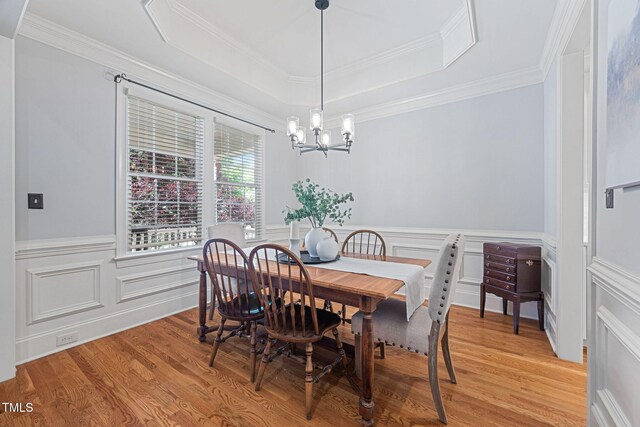 dining area with crown molding, a raised ceiling, light wood finished floors, and a chandelier
