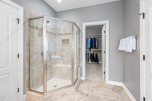 bathroom featuring baseboards, a shower stall, and a walk in closet