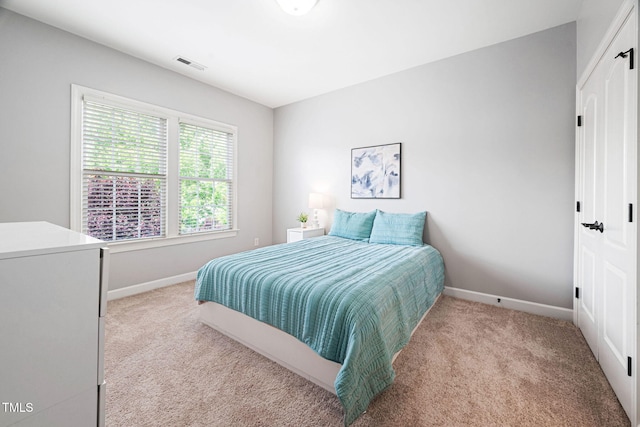 bedroom featuring a closet, baseboards, light colored carpet, and visible vents
