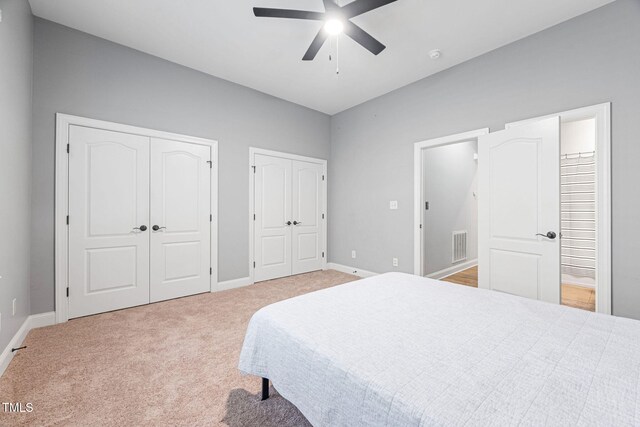 bedroom with connected bathroom, light carpet, two closets, baseboards, and visible vents